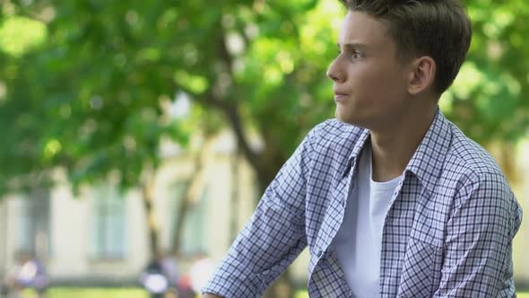 Teenage Couple Sitting Apart on Bench in Park, First Difficulties in Relations alt