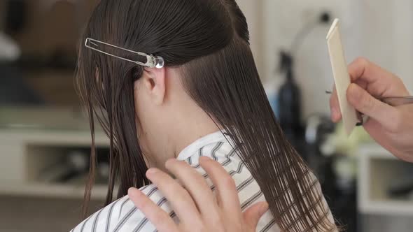 Hairdresser-stylist is cutting hair of a girl client