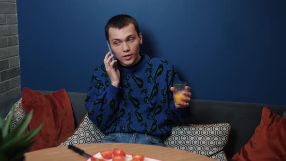 Handsome Caucasian Man Sitting in Kitchen Distracted From Food Cooking Talking on Smartphone alt
