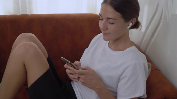 A Woman with a Smartphone Sitting on the Couch at Home Talking on the Phone