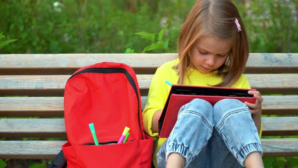 Girl Sits on Bench in Schoolyard and Does Homework alt