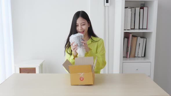 Young asian woman walking and unpacking of parcel box with online shopping while satisfied. alt