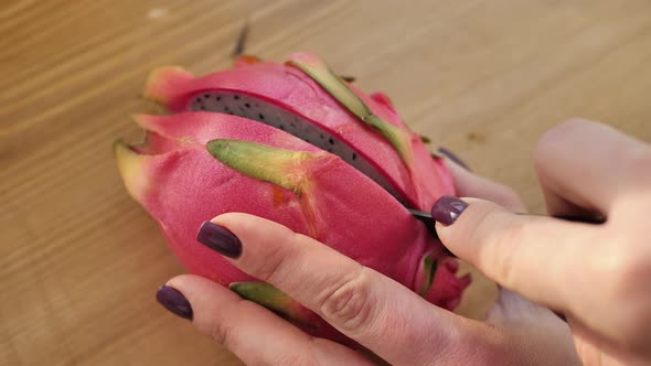 Closeup of Hands Cutting a Pitahaya Fruit with a Black Knife on a Wooden Board