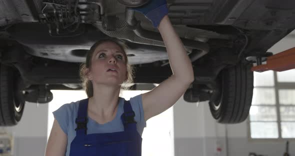 Confident female mechanic in a repair shop, she is working under a car, women's employment concept