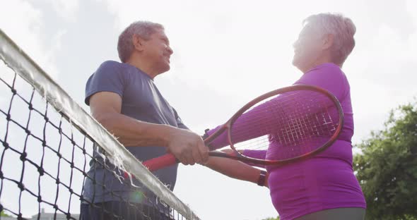 Video of happy biracial senior couple embracing on tennis court alt