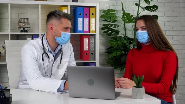 Doctor and patient wear protective masks on faces in hospital office talk listen alt