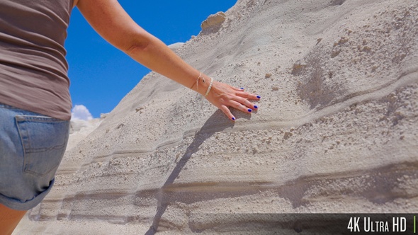 4K Closeup of woman hand touching white sandy texture rock wall formation at Sarakiniko, Greece alt