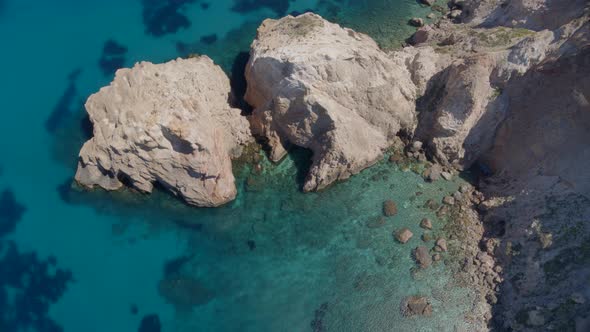 Top Down Aerial Zoom Out of Cliffs Cascading into the Blue Aegean Sea in Milos alt