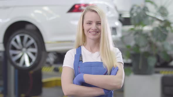 Portrait of Young Caucasian Woman Standing at the Background of White Car in Repair Shop. Blond alt