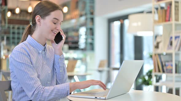 Young Businesswoman Talking on Smartphone with Laptop in Cafe alt