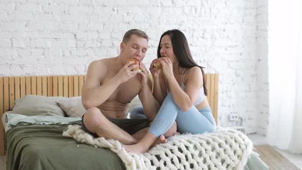 Sporty Young Man and Woman Are Eating Hamburgers Together After Workout at Home