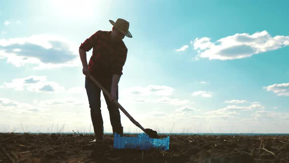 Farmer Digging Soil with Shovel in Rubber Boots in Garden Field at Sunset Spring alt