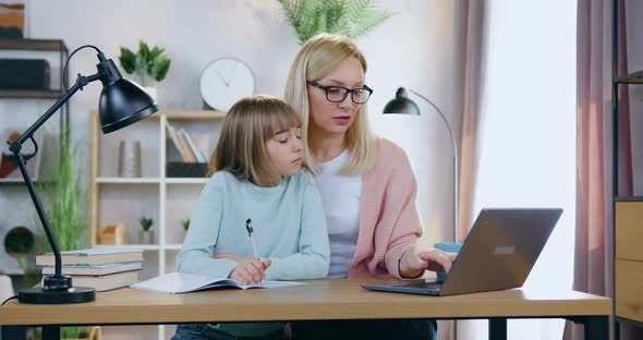 Mother in Glasses Sitting Together with Her 12-Aged Cute Daughter and Helping Her with Home Task alt