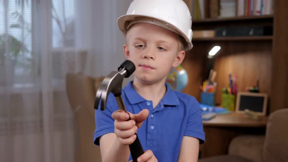 Portrait of a Little Boy in a White Helmet with a Hammer in His Hands at Home alt