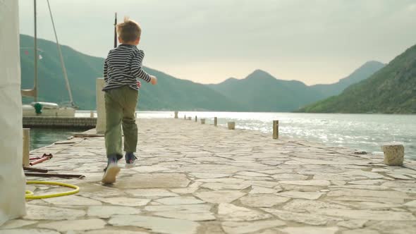 The Boy Runs Along the Pier Against the Backdrop of the Sea and Mountains