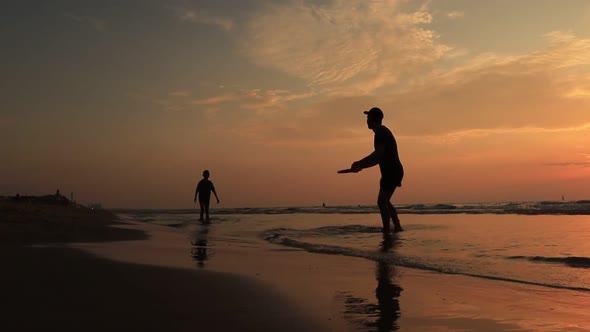 Father and Son Playing Frisbee Together in Shorts at Sea Sunset