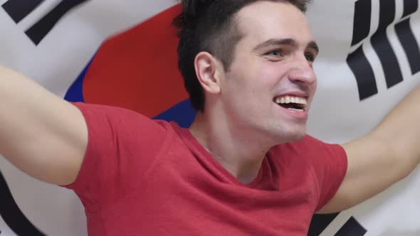 South Korean Man Celebrating while Holding the Flag of South Korea alt
