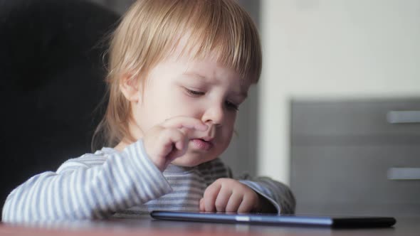 Portrait of a Child Sitting at a Desk and Enthusiastically Looking and Tapping the Screen of a