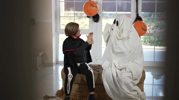 Happy Boy and Ghost Playing Hand Clapping Game Sitting Indoors in Living Room alt