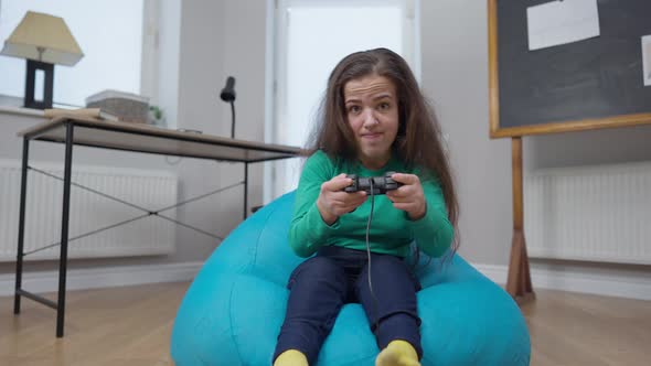 Female Gamer Rejoicing Winning in Online Video Game Sitting on Bag Chair Indoors alt