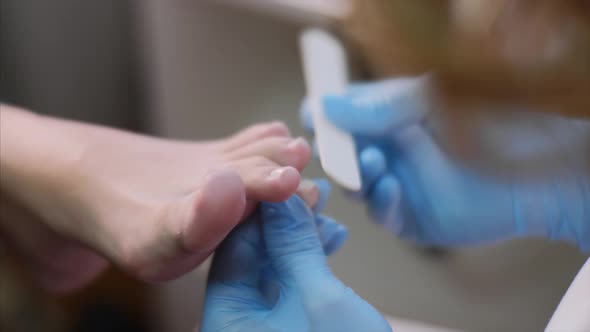 Pedicurist is Modeling Nails on Client's Toes Using Nail File in Beauty Salon