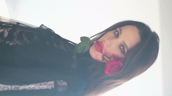 Vertical Video Glamorous Brunette Woman with Makeup for Halloween Rose Flower in Her Mouth alt