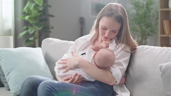 Mom Breastfeeds Her Little Daughter in the Morning Sun in the Living Room alt
