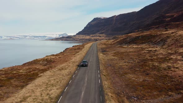 Drone Tracking Car Driving By Fjord Away From Mountains alt