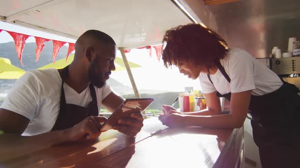 African american couple wearing aprons using digital tablet and taking notes in the food truck alt