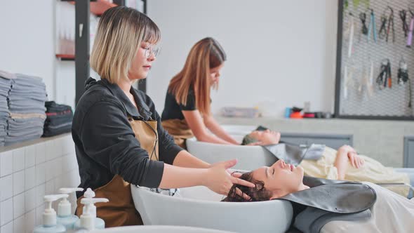 Asian young woman lying down on salon washing bed getting hair washed in hair salon by stylist. alt