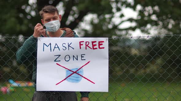 A Poster on the Fence with the Inscription Mask Free Zone. A Young Male Activist Comes Up and Takes alt