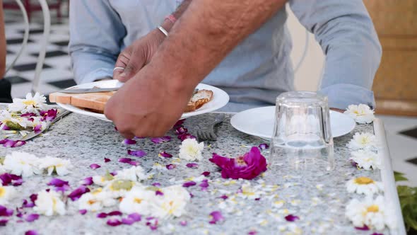 Waiter brings breakfast to a couple sitting at the table covered with flowers.