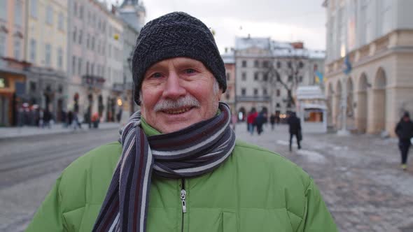 Portrait of Old Senior Man Tourist Smiling Looking at Camera in Winter City Center of Lviv Ukraine alt
