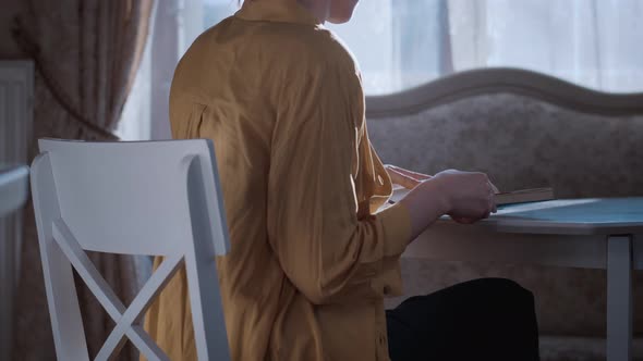 Girl Sits at Home and Reads a Book Near the Window in the Evening at Sunset alt