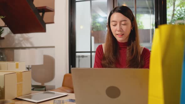 Young Asian woman use laptop to work in workplace room with many cartons or boxes
