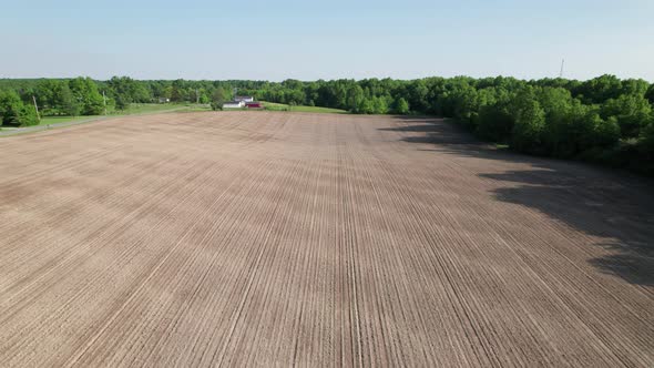 Aerial view of farm house and farm field with rows of plants under brght blue sky alt