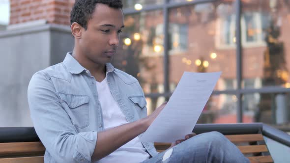 African Man Reading Documents while Sitting Outdoor alt