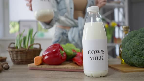 Soy Milk and Cow's Milk on Table in Kitchen with Female Hand Choosing Healthful Nondairy Drink alt