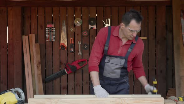 Carpenter Holds Two Wooden Beams in Hands and Compares Their Sizes alt