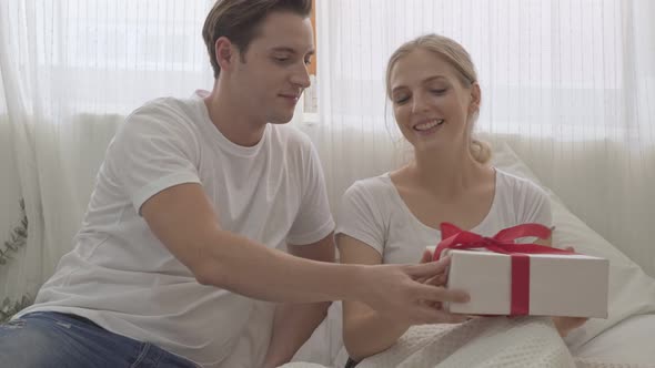 Man giving present box to his girlfriend on a bed alt