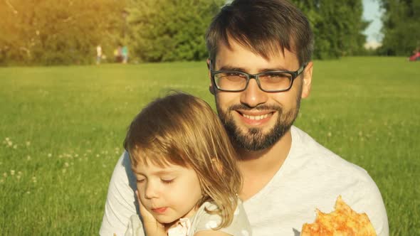 Father and Little Child Eat Pizza Outdoors Sitting on Lawn