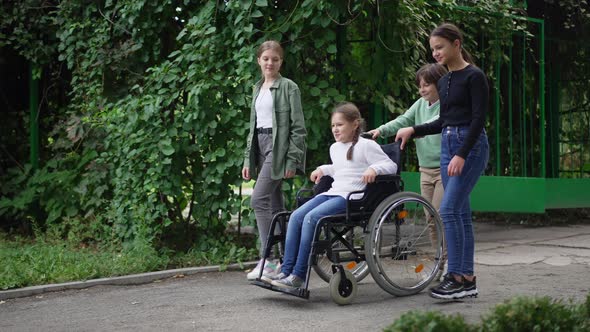 Group of Children Pushing Wheelchair with Disabled Friend in Slow Motion Outdoors alt