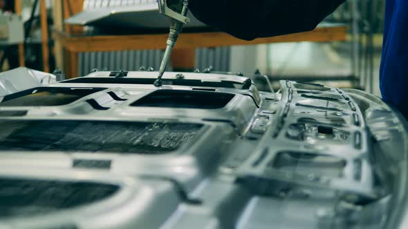 Factory Worker Applying Glue on a Car Part. Factory Facility Interior, Industrial Equipment alt