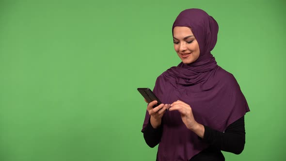 A Young Beautiful Muslim Woman Takes Selfies with a Smartphone  Green Screen Background