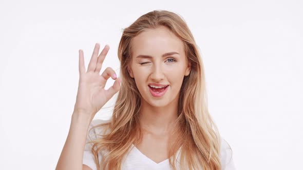 Young Beautiful Caucasian Blonde Girl Showing Ok and Smiling on White Background in Slowmotion alt