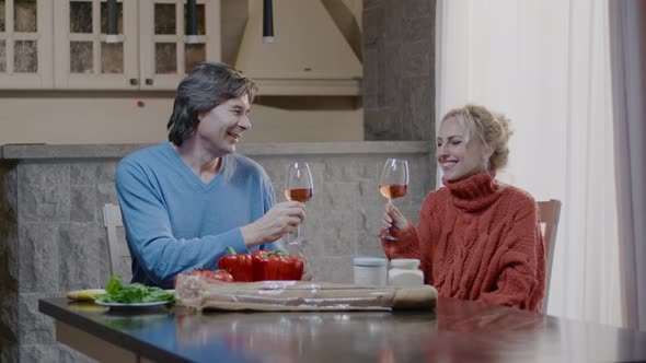 Handsome man and blonde woman with a glass of wine have dinner in the kitchen at home. alt