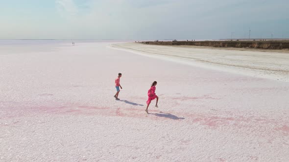 Aerial Drone Footage of Happy Young Couple in Pink Wear Having Fun and Joyfully Running on White alt