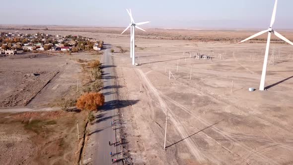 Cyclists Ride Along Road with a View of Windmills. alt
