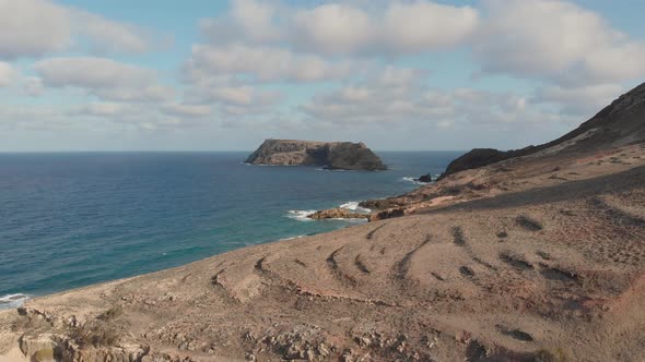 The northern cliff edged shore of Porto Santo and a remote road with another island in the distance. alt