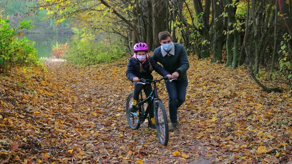 A young father teaches his daughter to ride a Bicycle in a protective helmet.